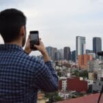 Mężczyzna fotografuje panoramę miasta smartfonem na statywie z dachu