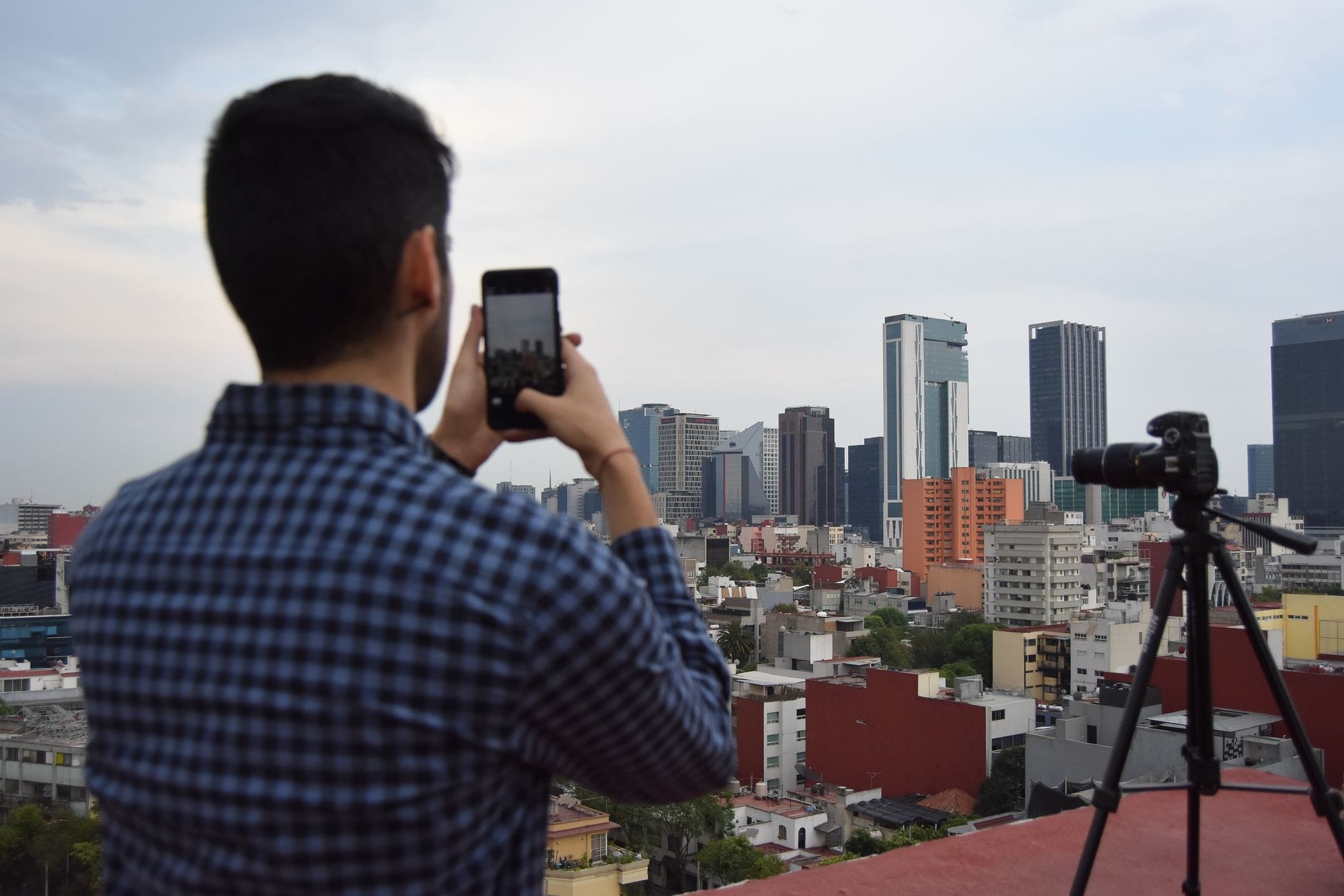Mężczyzna fotografuje panoramę miasta smartfonem na statywie z dachu