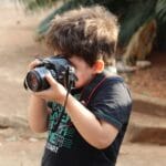 Młody chłopak z lustrzanką uczy się fotografii w plenerze