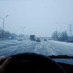Samochód jedzie o zmierzchu po oblodzonej, zaśnieżonej drodze z ruchem