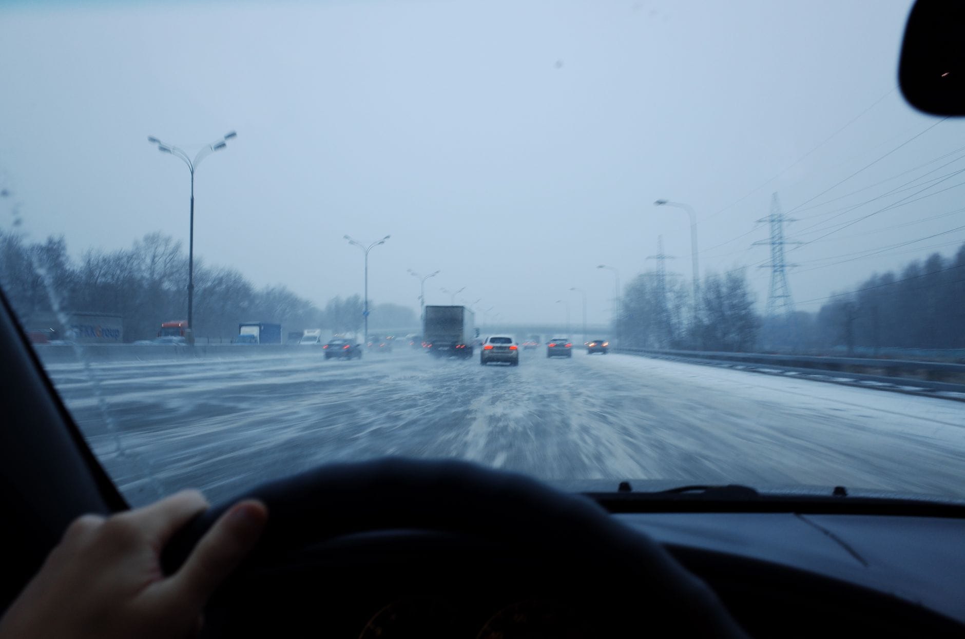 Samochód jedzie o zmierzchu po oblodzonej, zaśnieżonej drodze z ruchem